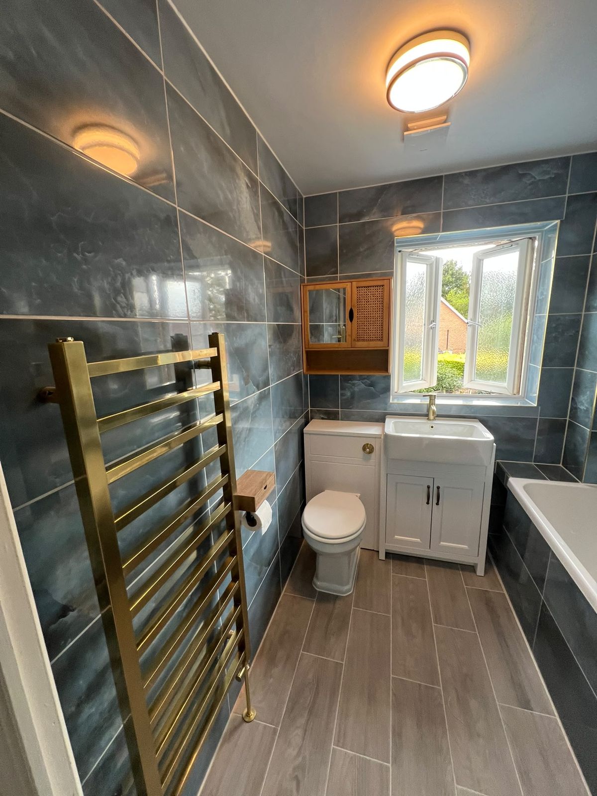 Finished bathroom with brushed brass towel radiator and slate-effect tiles